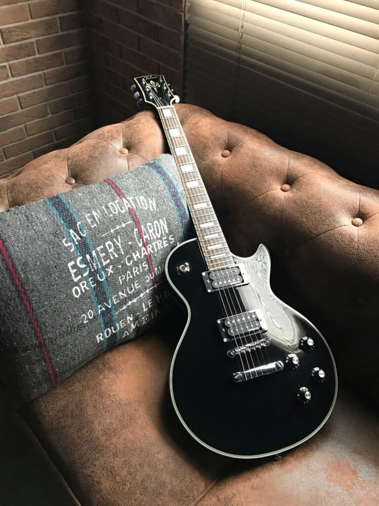 pexels-photo-2105038-2105038 A sleek black electric guitar rests on a chic leather sofa with a decorative pillow.